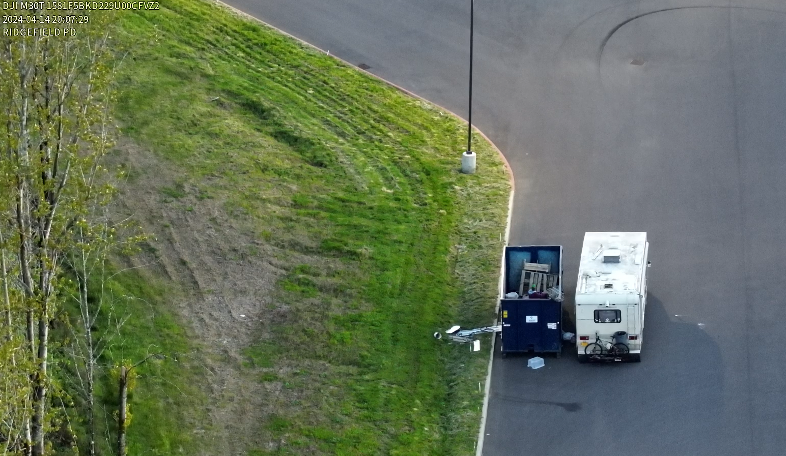 Aerial image of a large dumpster on black top with a subject in the dumpster.
